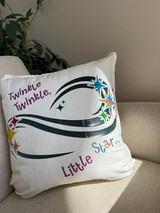Image of a white pillowcase a logo that reads “Twinkle Twinkle Little Star”, positioned above and below several different colored starshaped designs all connected by an organic, swirl-like shape using navy blue Twinkle.