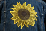 Close up of an image showing the back of a blue denim jacket using StripFlock Pro brown for the center of the sunflower design and Glitter gold for the petals.