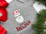 Image of a gray baby onesie with a Santa’s beard and hat using white StripFlock Pro with red/white Buffalo Plaid Pattern for parts of the Santa hat and the words “Santa’s Little Helper” using red Glitter underneath the design.