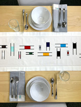 Image of a linen-colored table runner with a Piet Mondrian-like design shopping symmetrical color blocks using Stripflock Pro with place settings and cutlery surrounding the table runner.