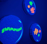 Image of three small round canvases appearing blue in the dark; different colors of Easy Glow Heat Transfer Vinyl depicting several fish and one canvas that reads “Swimming”.