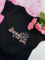 Image of a black onesie on to of pink gauze and pink flowers to the side with a logo “Sweet on you” with a logo of “ice cream, muffin and candy” incorporated using the Brown Polka Dot Pattern and Glitter around the letters .
