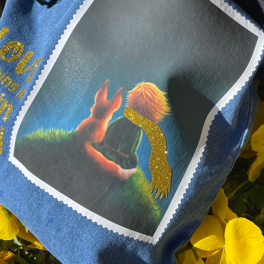 Closeup image of a denim bag with a logo of “The Little Prince and Fox sitting” using EasyColor DirectToVinyl and Gold Glitter.