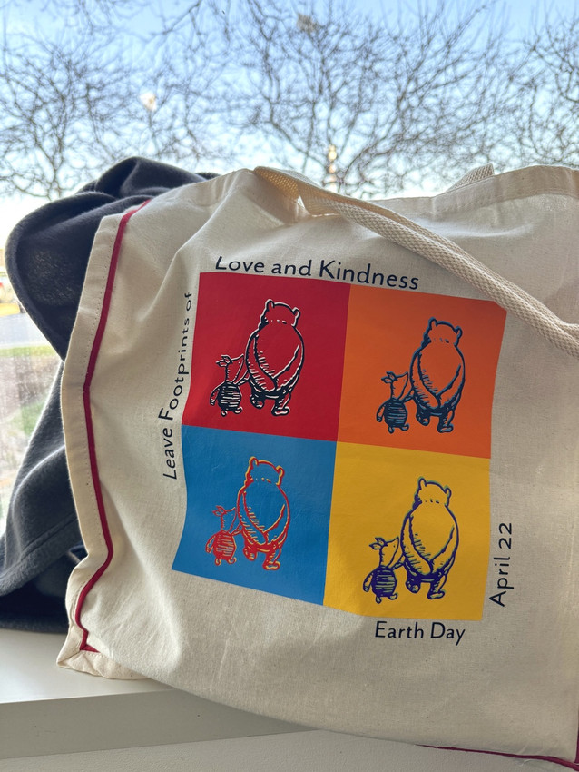 Partial Image of a natural colored, red-piped shopping tote with logo of “Winny the Pooh and Piglet” in four different colored squares using warm colors of EasyWeed EcoStretch and the words “Leave Footprints of Love and Kindness – Earth Day April 22”.