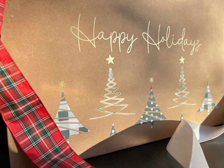 Closeup of a brown gift bag with the logo of “Happy Holidays” and “Five Christmas Trees” aligned across the bottom of the bag using the Sage Buffalo Plaid and Polka Dot Pattern alternately with splashes of Rose Gold EasyWeed Electric.