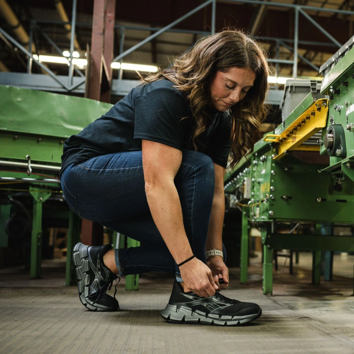 Female worker in a manufacturing setting kneeling to tie her women's safety shoes in style rb140.