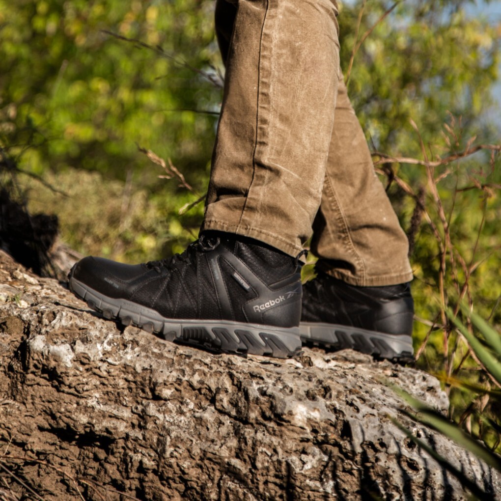 Closeup of landscaper standing on uneven terrain in Reebok yard work shoes. 