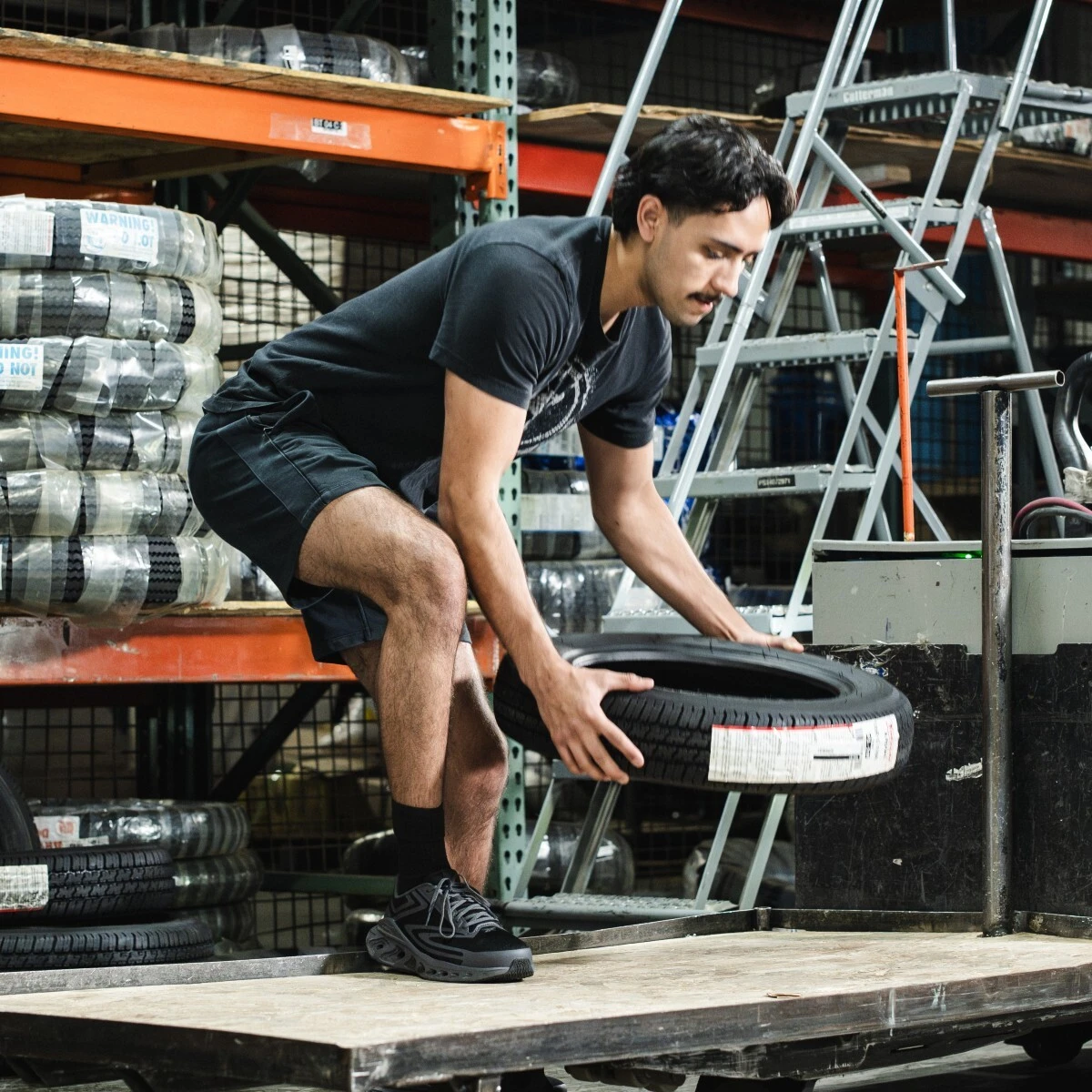 Male worker placing heavy tire on a loading bed in a warehouse wearing men's safety shoe rb3631.