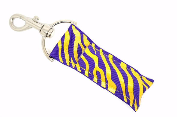 Zebra Royale Lippy Clip - Purple Yellow Gold Glitter Zebra Lip Balm Holder

Go bold or go home. The Zebra Royale lip balm holder is fierce, fun, and fabulously flashy with its striking purple and yellow background and dazzling gold glitter zebra stripes.

Perfect for wild hearts and style queens, this eye-catching lippy clip adds a glam pop to your keys, bag, or backpack. Because your lip balm deserves to travel in style.

Why You’ll Love It:
Unique purple and yellow combo with sparkling gold zebra print
Easy-to-use clip attaches to keys, purses, and backpacks
Keep your balm secure and always within reach
A bold gift for anyone who loves glam with attitude
Handmade with high-quality printed fabric
Product Details:

Design: Purple and yellow background with gold glitter zebra stripes

Material: High-quality printed fabric

Clip: Strong silver lobster clasp

Fits: Standard-size lip balm tubes

Includes: 1 Zebra Royale lip balm holder (lip balm not included)

Exclusively Handmade by Gettin Lippy in the USA