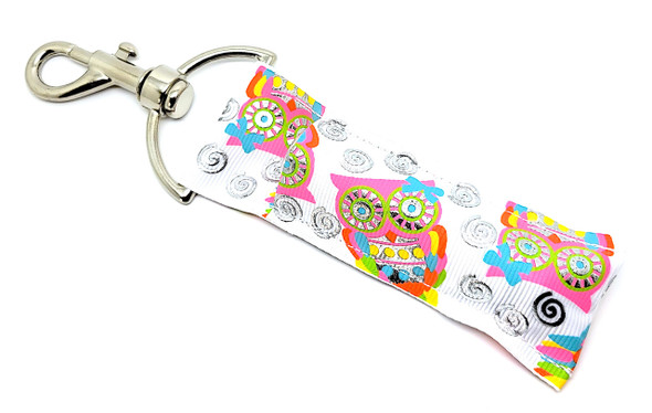 Whimsy Watch – Owl Lip Balm Holder with Silver Foil & Dial Eyes

Meet Whimsy Watch, your next favorite lip balm holder that’s as functional as it is fabulously fun! This eye-catching design features playful, cartoon-style owls with bright pink, orange, yellow, and teal feathers, complete with teal ribbon bows on their heads and quirky, wind-up style dial eyes.

Set on a crisp white background with shimmering silver foil squiggles, this lip balm keychain delivers both style and shine. Whether you're clipping it to your purse, backpack, or keys — it’s bound to turn heads and spark smiles!

Why You'll Love It:

Eccentric Owl Design
The charming wind-up owl faces, dial eyes, and glittering accents make this a whimsical favorite for kids and grownups alike.

Always Within Reach
Thanks to the secure swivel clip, you’ll never lose your lip balm in the bottom of your bag again!

Durably Handmade
Crafted in the USA with high-quality fabric, metallic detailing, and sturdy stitching for a long-lasting hold.

Gift-Worthy Quirkiness
Perfect for:

Owl lovers

Teachers & students

Birthday surprises

Quirky style fans

Holiday stockings

“Just because” gifts

Satisfaction Guaranteed
Love it or your money back — no questions asked.

Product Details:

Size: 6.5 inches (including clasp) x 1.5 inches

Material: Premium fabric with silver foil detail + high-quality metal clasp

Includes: 1 Whimsy Watch Owl Lip Balm Holder

Note: Lip balm not included — pair with any Gettin’ Lippy balm!

Handmade in the USA