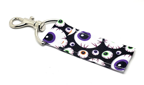 Spooky Eyeball Halloween Lip Balm Holder – Purple, Green & Orange Creepiness!

Dare to stand out this spooky season with our Halloween Eyeball Lip Balm Holder! Featuring a wickedly fun pattern of green, purple, and orange eyeballs on a dark background, this eerie-yet-adorable holder is the perfect Halloween accessory.

Whether you're building boo baskets, prepping for a Halloween party, or just love creepy-cute vibes, this lip balm holder is ready to turn heads (and eyes)! Clip it to your bag, keys, or backpack so your favorite balm is always on hand—and freakishly festive.

Why You’ll Love It:
Eye-Catching Halloween Design

Covered in spooky, colorful eyeballs, this holder is packed with personality. It's playful, bold, and just the right amount of creepy for Halloween lovers.

Keep It Close, Keep It Cute

Say goodbye to digging through your bag—just clip this on and go! The swivel-head clasp keeps your lip balm upright and within reach wherever you go.

Handmade in the USA

Made with care and quality craftsmanship, each holder is built to last through Halloween and beyond.

Great For:

Boo basket fillers

Halloween party favors

Teachers, coworkers, friends & teens

Trick-or-treat swaps

Fall fair prizes & seasonal giveaways

Lip balm lovers with a spooky side!

Buy With Confidence

Gettin’ Lippy Lip Balm Holders are customer-favorites for a reason—stylish, practical, and made with love. Your purchase is backed by our 100% Money-Back Guarantee—because spooky shouldn’t be stressful.

Product Details:

Dimensions: 6.5 inches (with clasp) x 1.5 inches

Includes: 1 Halloween Eyeball Lip Balm Holder

Note: Lip balm not included—pair with one of our seasonal lip balms for the full Halloween effect!

Handmade in the USA – Add a Creepy-Cute Touch to Your Fall Style Today!