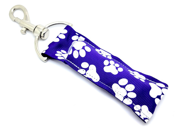Purr-fect Spirit – Purple Glitter Paw Print Lip Balm Holder Keychain

Show off your wild side or school pride with the Purr-fect Spirit lip balm holder! This purple beauty is covered in playful white cat paw prints — each accented with dazzling glitter that adds just the right amount of sparkle. Whether you're a proud pet parent, an animal lover, or want to match your school colors, this holder is as functional as it is adorable.

Clip it to your keys, backpack, or gym bag and keep your favorite chapstick handy wherever you go!

Why You’ll Love It:

Glittery Fun – Sparkly white paw prints pop against a bold purple backdrop

Pet & School Spirit Approved – Perfect for cat lovers or cheer squads

Always Handy – Never lose your lip balm again

Clip & Go – Attached keyring and clasp for convenience

Product Details:

Size: Approximately 6.5" x 1.5"

Material: High-quality printed fabric

Includes: 1 Purr-fect Spirit lip balm holder

Note: Lip balm not included

Handcrafted in the USA