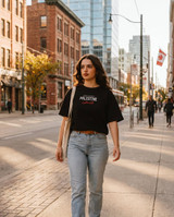 Black oversized t-shirt front with small white Palestine wordmark, coordinates and Arabic script on chest, worn on a city street