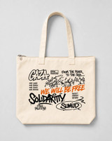 Model carrying the Sumud Graffiti Tote Bag over the shoulder, showing the cream canvas zip tote with black and orange graffiti-style Palestinian solidarity print
