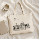 Lifestyle shot of the Al Quds Jerusalem Tote Bag laid on a linen surface beside a coffee cup and notebook