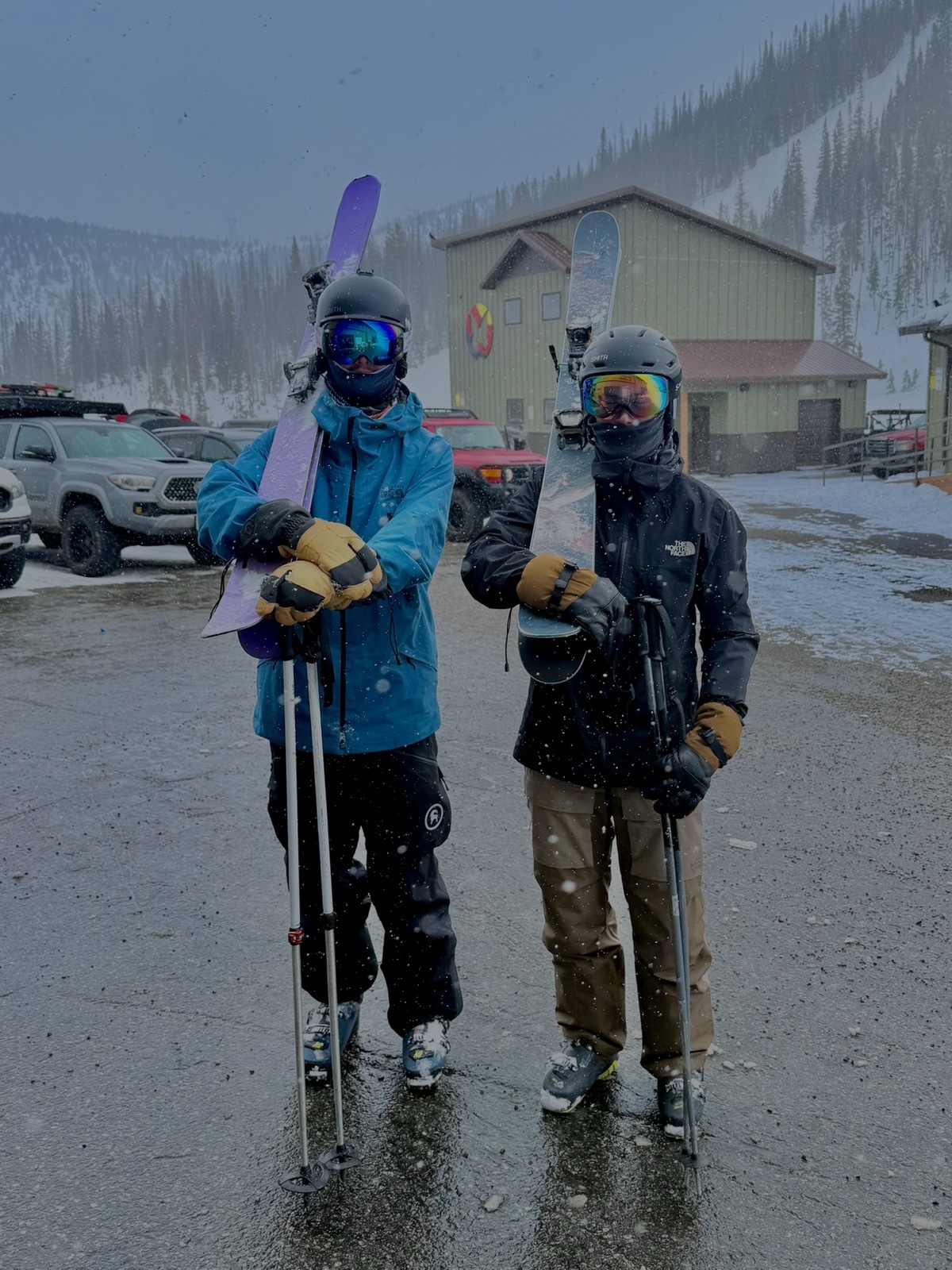 Two skiers holding skis on a snowy mountain day