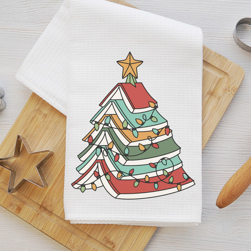 Book Christmas tree kitchen towel flat lay on wooden cutting board — colorful stacked books forming Christmas tree with star and lights on white waffle weave