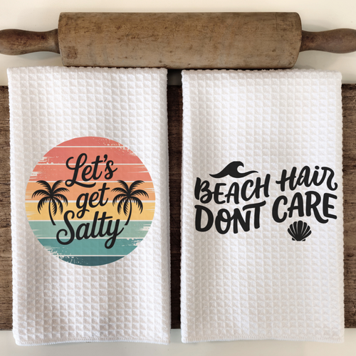 Beach kitchen towel set featuring Let's Get Salty retro sunset design and Beach Hair Don't Care bold typography, sublimation printed white waffle weave dish towels hanging on rustic wooden rack.
