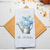 Personalized white waffle weave kitchen towel printed with a watercolor blue hydrangea bouquet in a galvanized watering can and custom family name in navy script, styled on a wood cutting board.