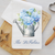 Personalized white waffle weave kitchen towel printed with a watercolor blue hydrangea bouquet in a galvanized watering can and custom family name in navy script, styled on a wood cutting board.
