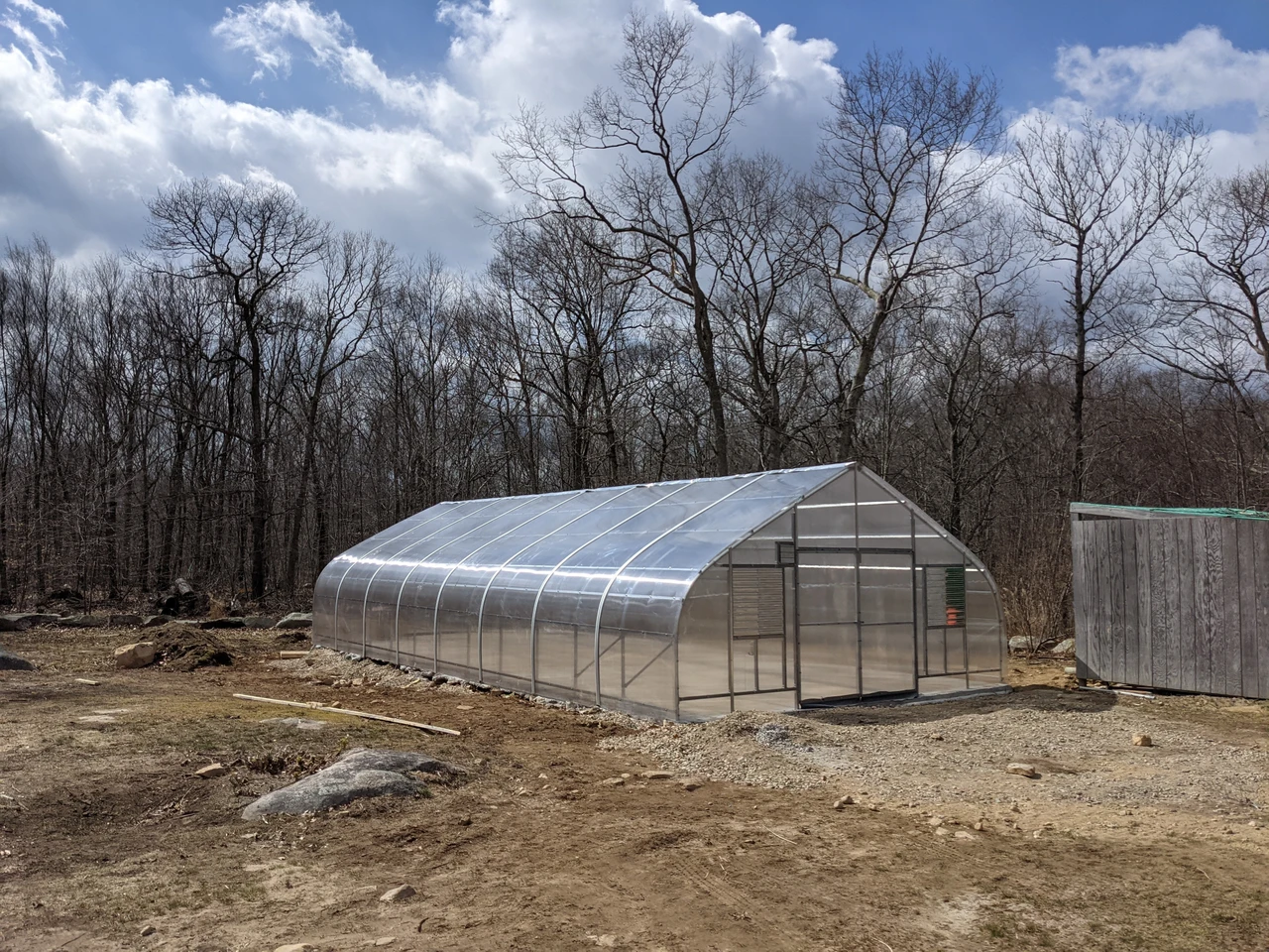 A covered greenhouse beside a wooded area.