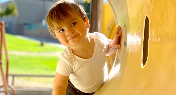 Toddler smiling through yellow playground tube