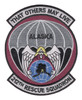 Shield-shaped embroidered patch with gray and burgundy field, winged angel descending with parachute at center, blue globe with Alaska state silhouette and "ALASKA" text, and scrolls reading "That Others May Live" at top and "212th Rescue Squadron" at bottom.