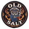 Round 4-inch embroidered Old Salt patch on black background featuring a bearded captain skull in naval cover with crossed anchors, smoking pipe, gold rope border, and 'Est. At Sea' inscription in gold lettering with merrowed edge border.