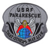 Badge-shaped embroidered patch with gray and silver field, black border, "USAF PARARESCUE" at top, angel with gold halo in red cloak kneeling over a blue and green globe, parachute canopy above, and scroll "That Others May Live" at bottom.