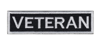 Black rectangular tab patch with the word VETERAN in white block capitals inside a white stitched border.