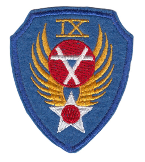 Shield-shaped embroidered patch with royal blue field, gold Roman numeral IX at top, spread gold wings flanking a red circular device with white diagonal lines, and a white five-pointed star at the base.