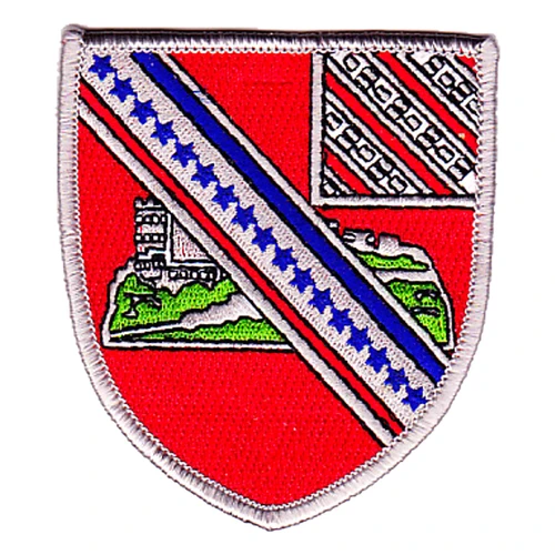 Red shield-shaped 17th Field Artillery Regiment patch with a castle on a green mount crossed by a silver band of blue stars and a striped canton in the corner, inside a silver merrowed border.