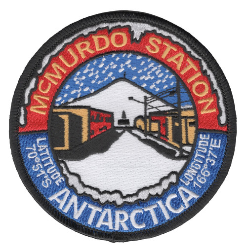 Round McMurdo Station Antarctica patch with white icicles over a red arc, station buildings and a snowy peak under falling snow, blue lower half and black merrowed border.