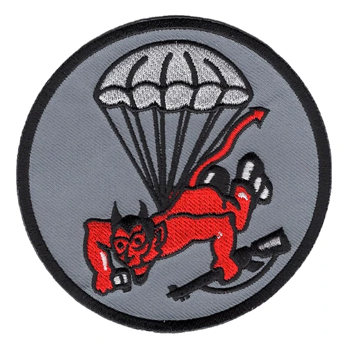 Round gray patch with a black border showing a red horned devil in black jump boots descending under a white parachute with a rifle in one hand, the 508th Parachute Infantry Regiment Red Devil.