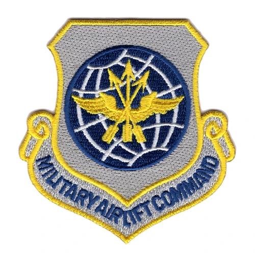 Silver gray Air Force major command shield with a dark blue gridded globe, a gold eagle over three rising arrows, and MILITARY AIRLIFT COMMAND lettered across the scroll below.