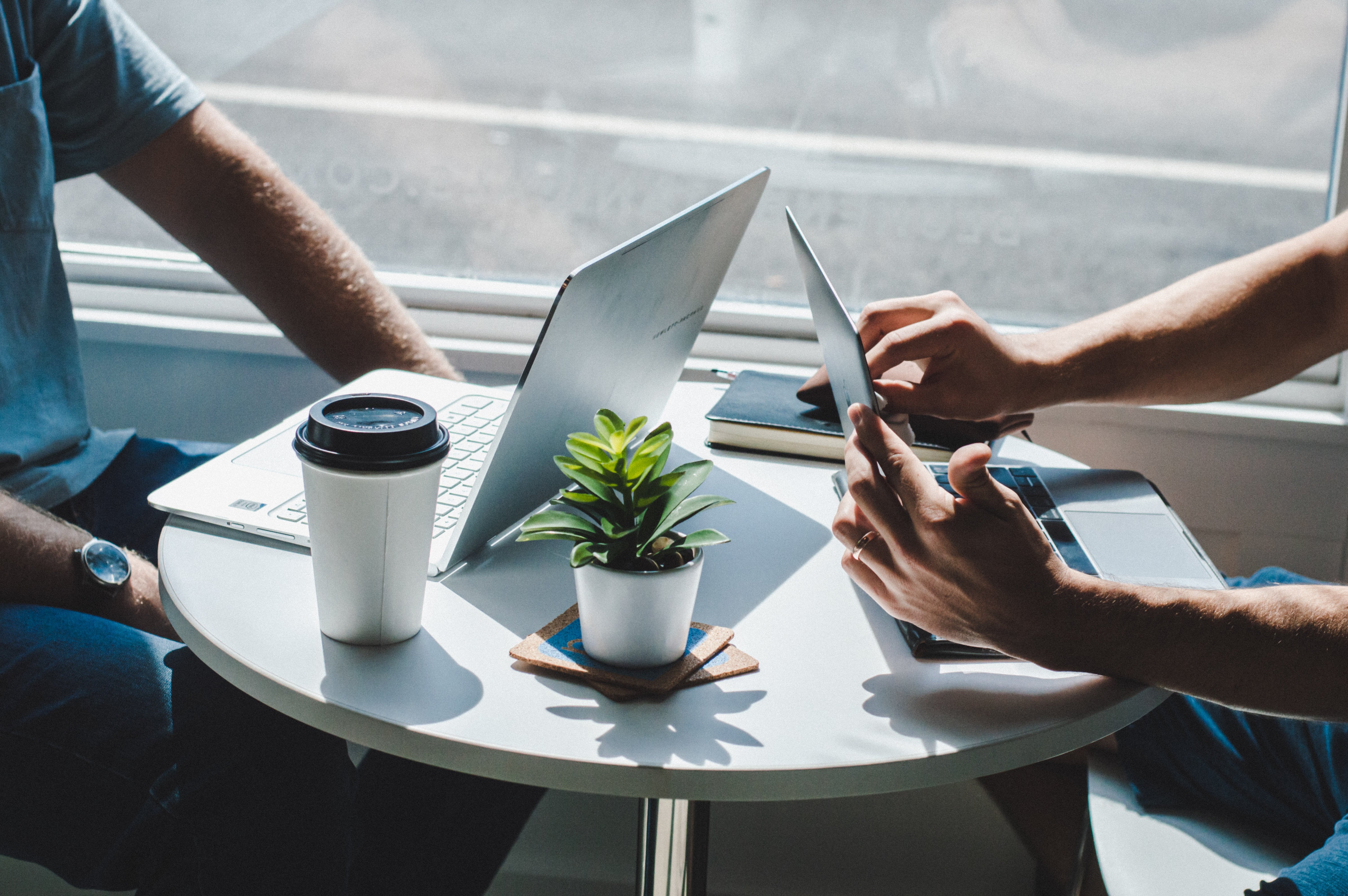  Two individuals working at a small round table with laptops and a tablet.