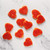 Heart-shaped sugar cookies coated in sparkling red sugar scattered across a white marble surface.