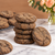 Stack of dark gingerbread latte cookies coated with a light sugar, espresso, and ginger mixture, displayed on parchment over white marble with fresh flowers in the background.