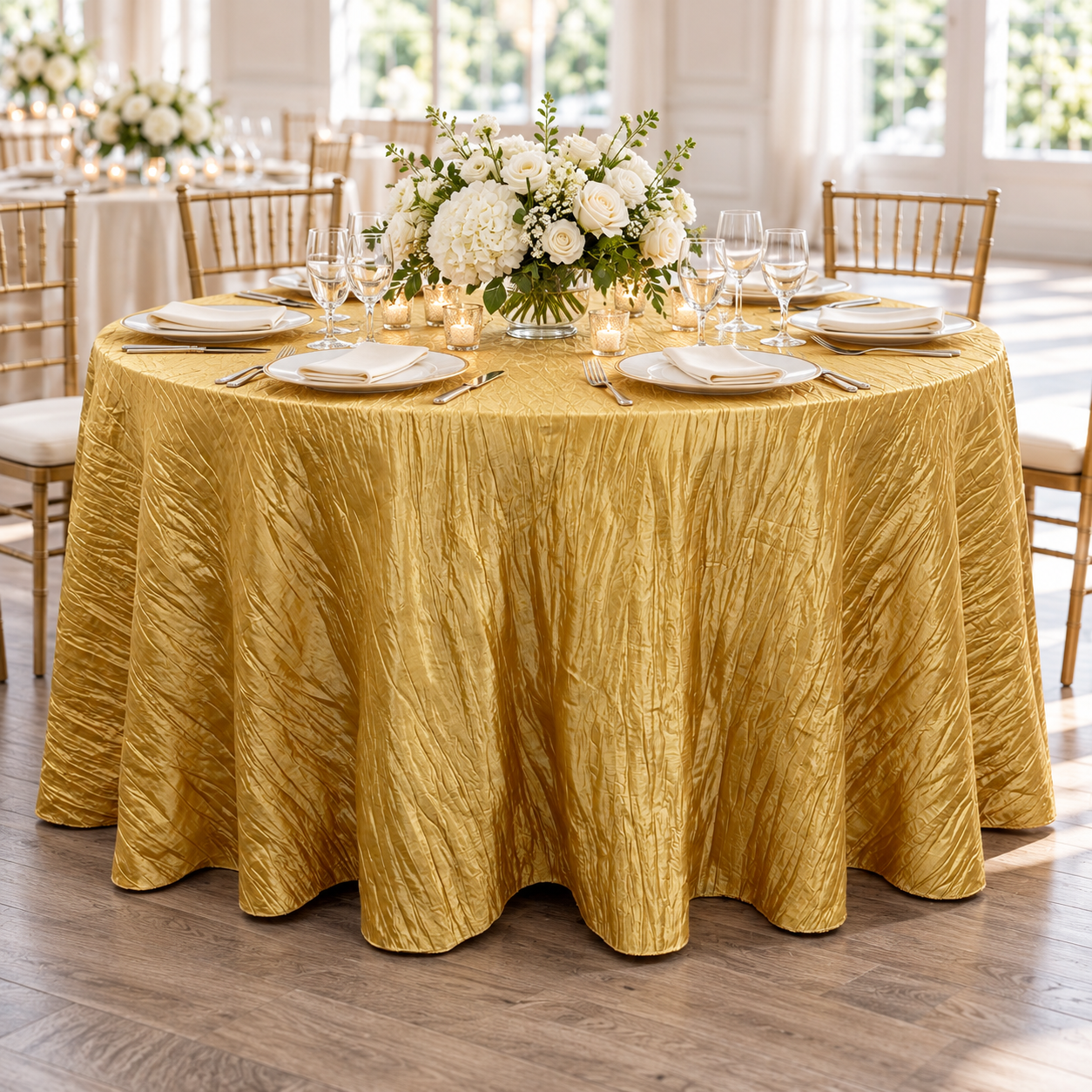 Gold crinkle taffeta round tablecloth styled with white flowers, plates and clear glassware.
