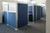 Row of office cubicles with blue fabric panels and frosted upper sections in a modern workspace.