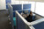 Overhead view of a person working at a desk inside blue-panel office cubicles near large windows.