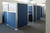 Row of office cubicles with blue fabric panels and frosted upper sections in a modern workspace.