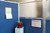 Office cubicle corner with blue panels, a frosted glass divider, a wall calendar, and a small plant on a cabinet.