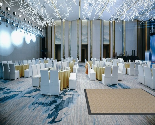 Elegant banquet hall with round tables, white chair covers, gold table linens, and overhead decorative lighting.