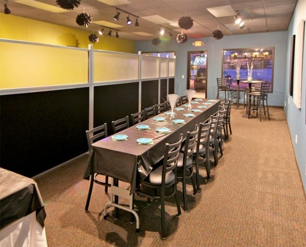 Long banquet table set with plates and chairs inside a restaurant event space with modular wall dividers.
