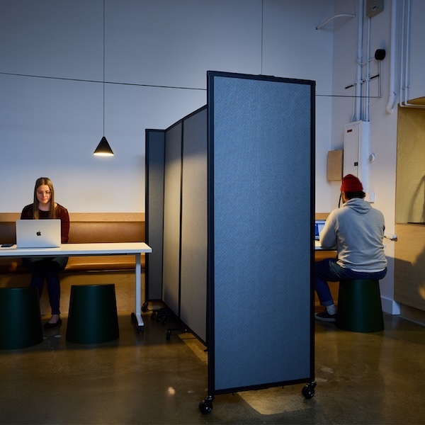 Two people working at desks separated by a rolling privacy screen in a modern workspace.