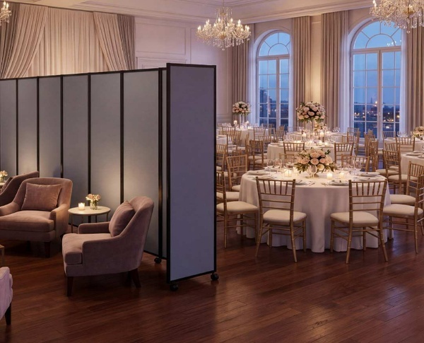 Elegant wedding‑style banquet room with round tables, chandeliers, and a freestanding room divider separating a lounge area.
