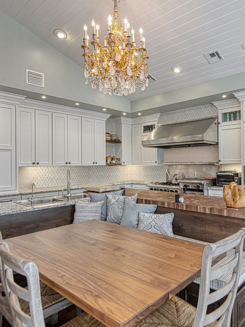 Unique neutral patterned handmade tile backsplash with butcher block island, eat in kitchen table, and gold chandelier