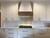 Beautiful White Farmhouse Kitchen with Decorative Tile Backsplash and Wooden Oven Hood Beautiful White Farmhouse Kitchen with Decorative Tile Backsplash and Wooden Oven Hood
