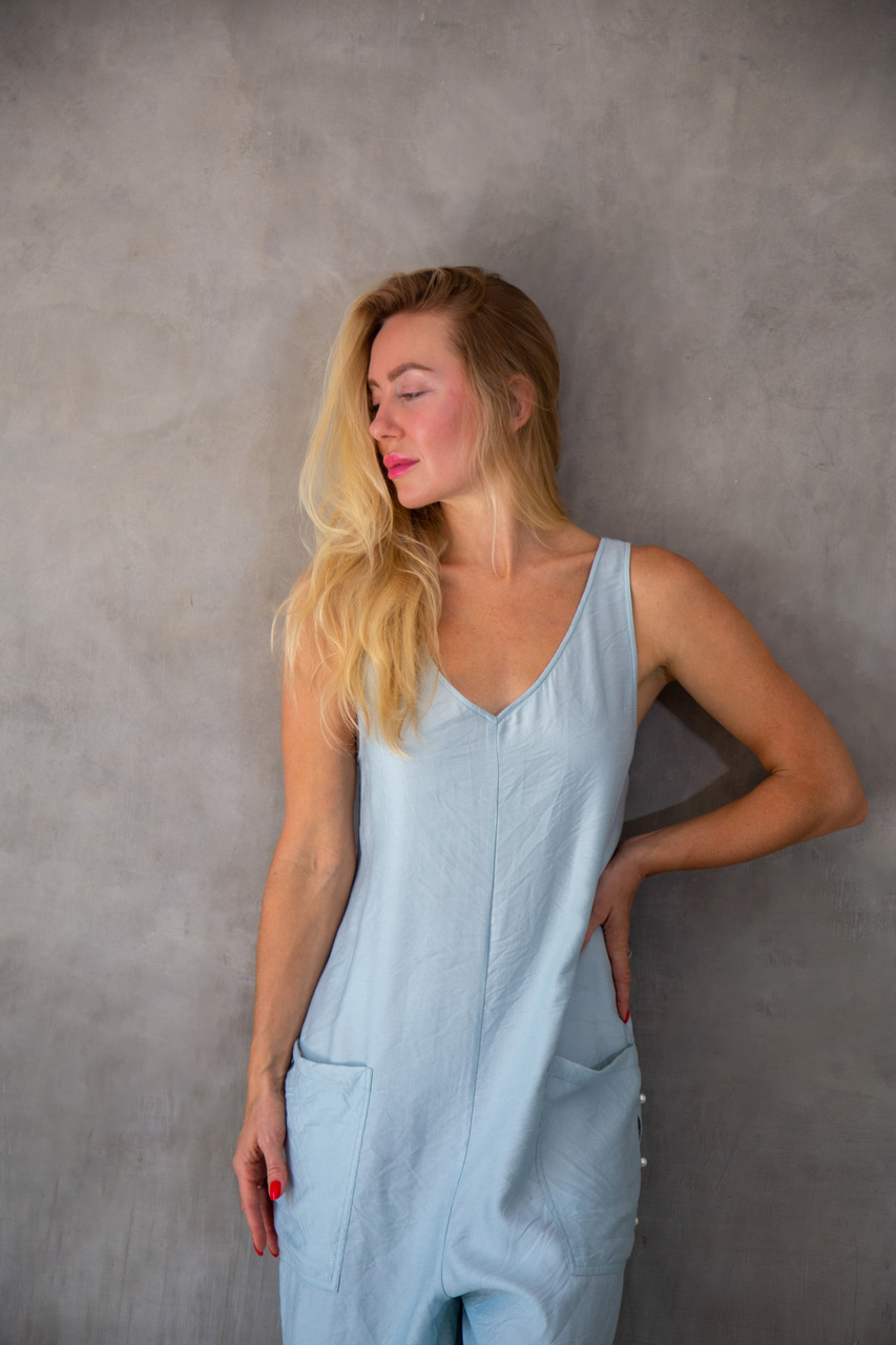 Model leaning against a wall in a powder blue adjustable jumpsuit, effortless casual elegance by Eluvare.